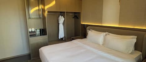 Una habitación de hotel con una cama grande, un vestidor amplio, una kitchenette pequeña y un baño.