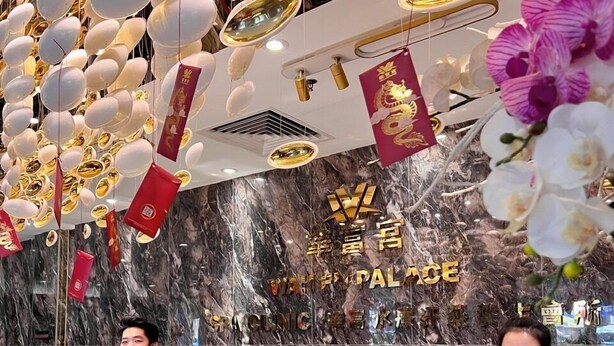 Un área de recepción con pared de mármol, mostrador de vidrio y elementos decorativos como adornos colgantes e insignias.