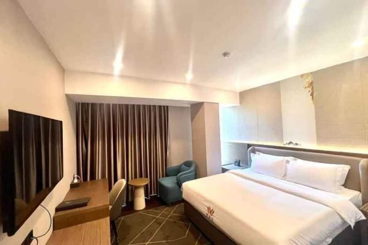 Une chambre d’hôtel avec un lit, un bureau, une chaise, une télévision et des rideaux.