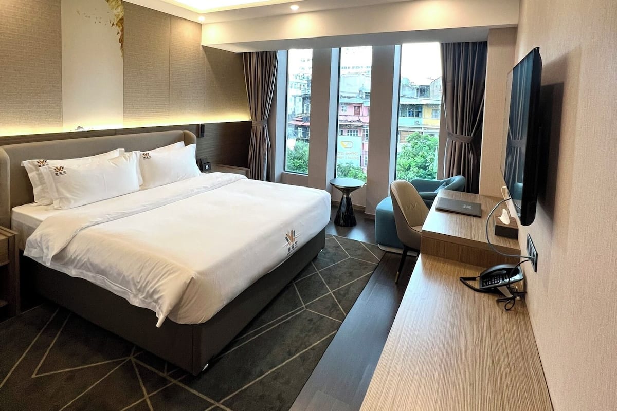 Une chambre d’hôtel moderne dotée d’un grand lit, d’un bureau avec une chaise, d’un téléviseur à écran plat et offrant une vue sur la ville grâce à de grandes fenêtres.