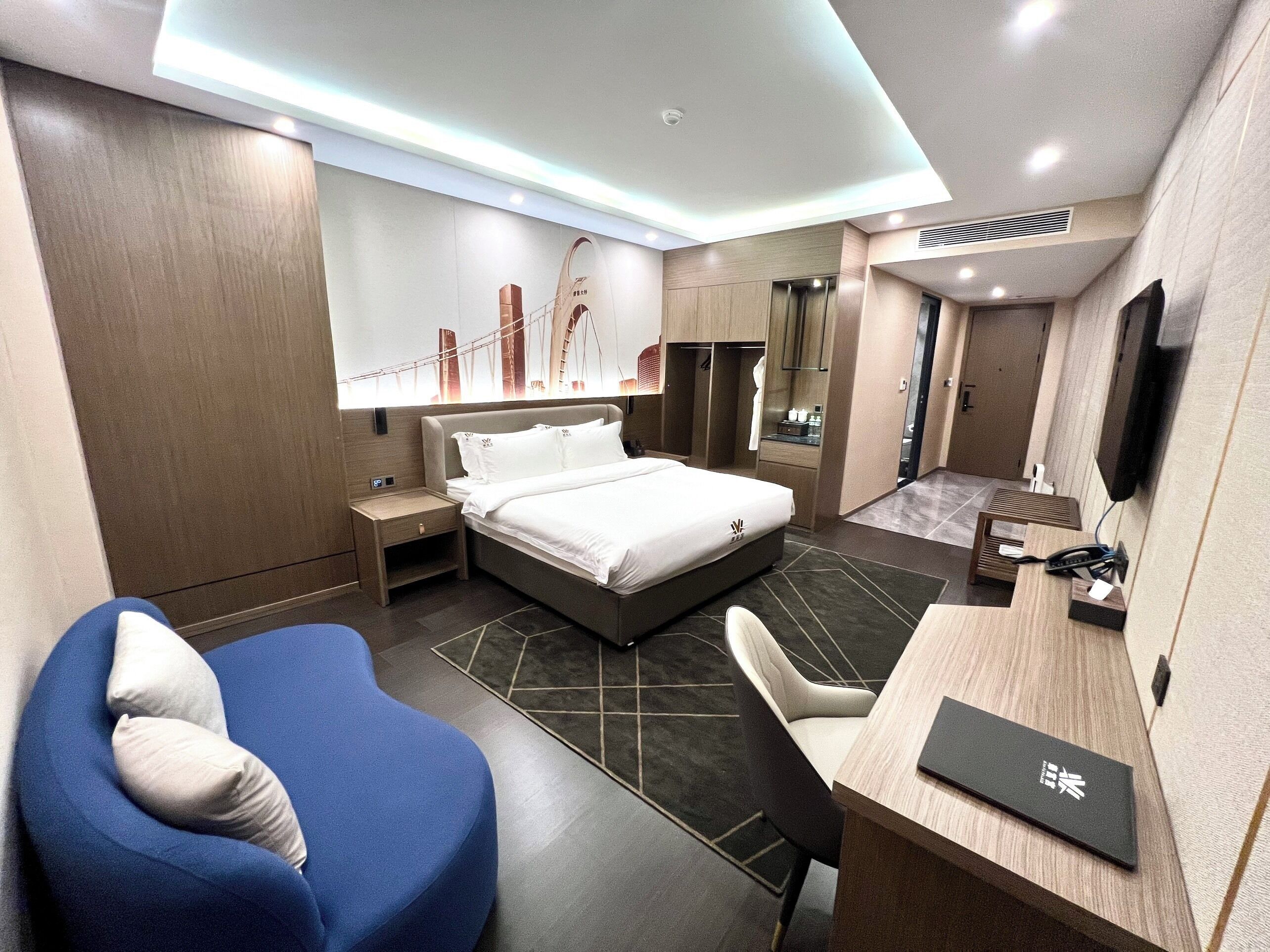 A modern hotel room with a bed, a desk, a chair, a TV, and a bathroom.