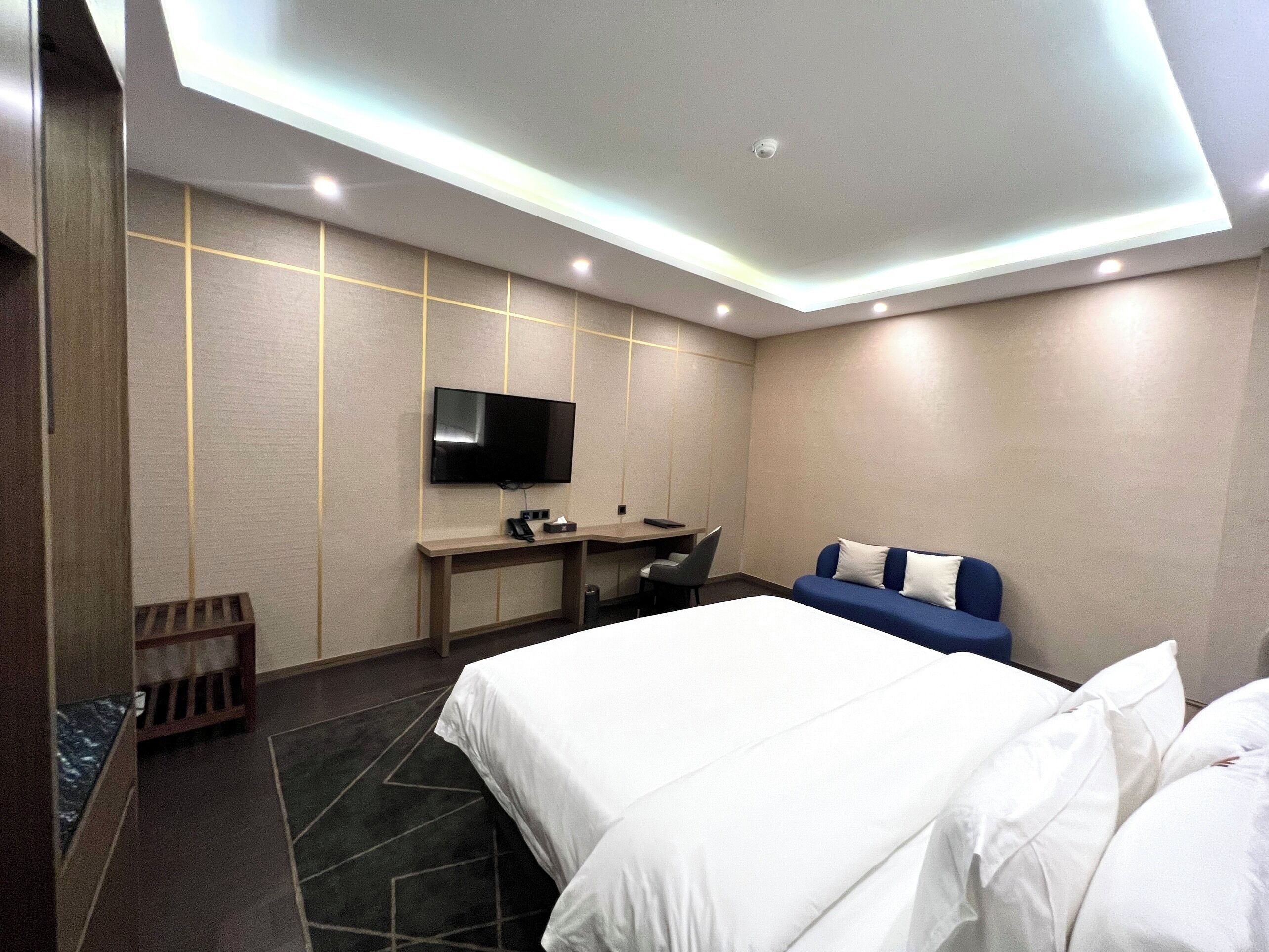 Habitación de hotel con cama, escritorio, silla, televisión y sofá azul.