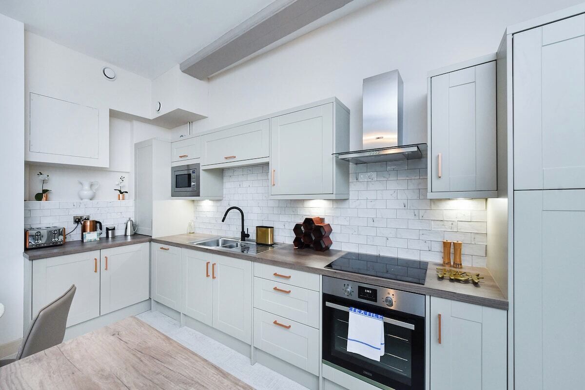 A modern kitchen with white cabinetry, a built-in oven, a microwave, and a stainless steel range hood.