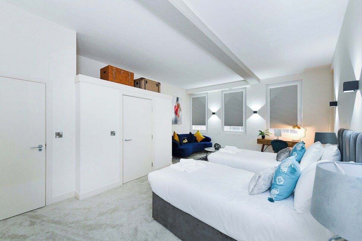 A modern bedroom with a large bed, a desk, a sofa, and a wardrobe.