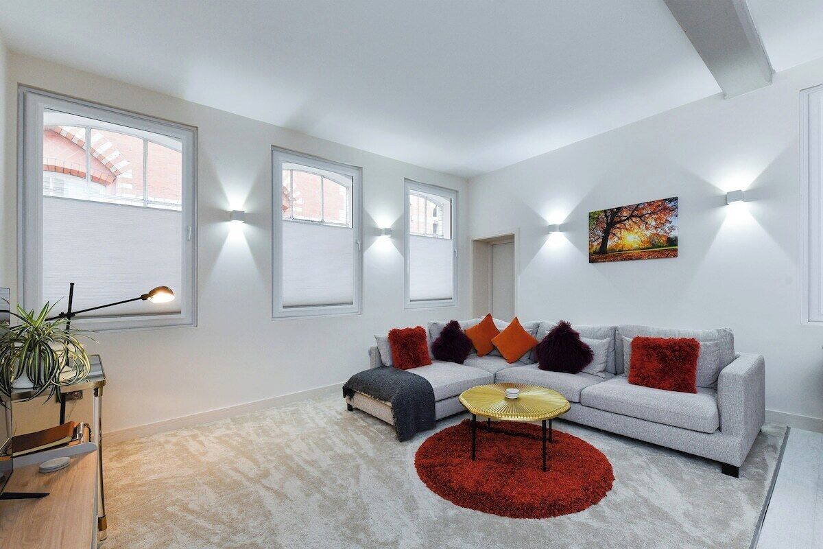 Ein modernes Wohnzimmer mit einem grauen Sofa, roten und orangefarbenen Kissen, einem runden Couchtisch und einem Bild an der Wand.