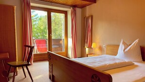 Una habitación de hotel con una cama de madera, un escritorio, una silla y un ventanal con cortinas.