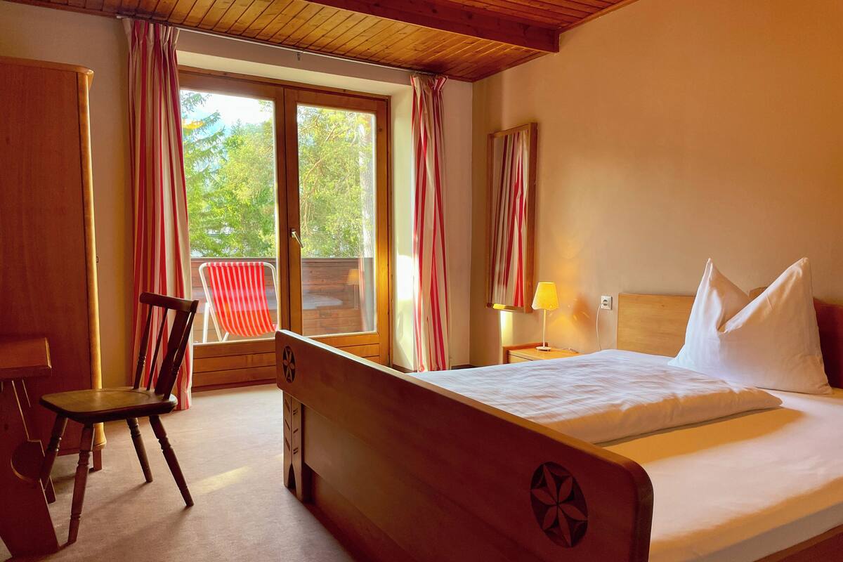 Una habitación de hotel con una cama de madera, un escritorio, una silla y un ventanal con cortinas.