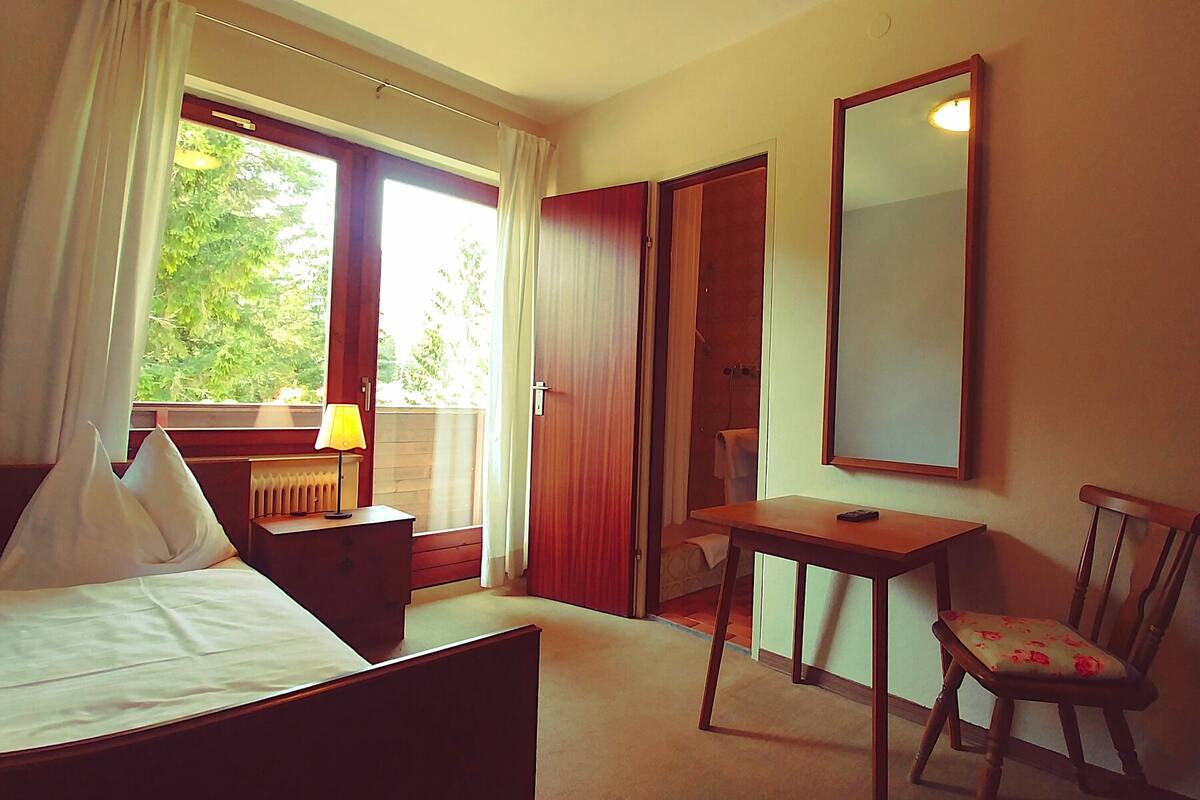 Habitación de hotel con cama, escritorio, silla, espejo y ventana con cortinas.