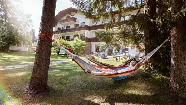 Una hamaca entre árboles en un patio con un edificio al fondo.