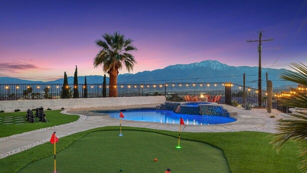 Un campo de golf con piscina, palmeras y montañas al fondo.