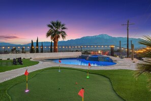 A golf course with a pool, palm trees, and mountains in the background.