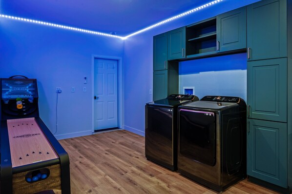 A laundry room with a washing machine and dryer, a wooden floor, teal cabinets, and LED strip lighting.
