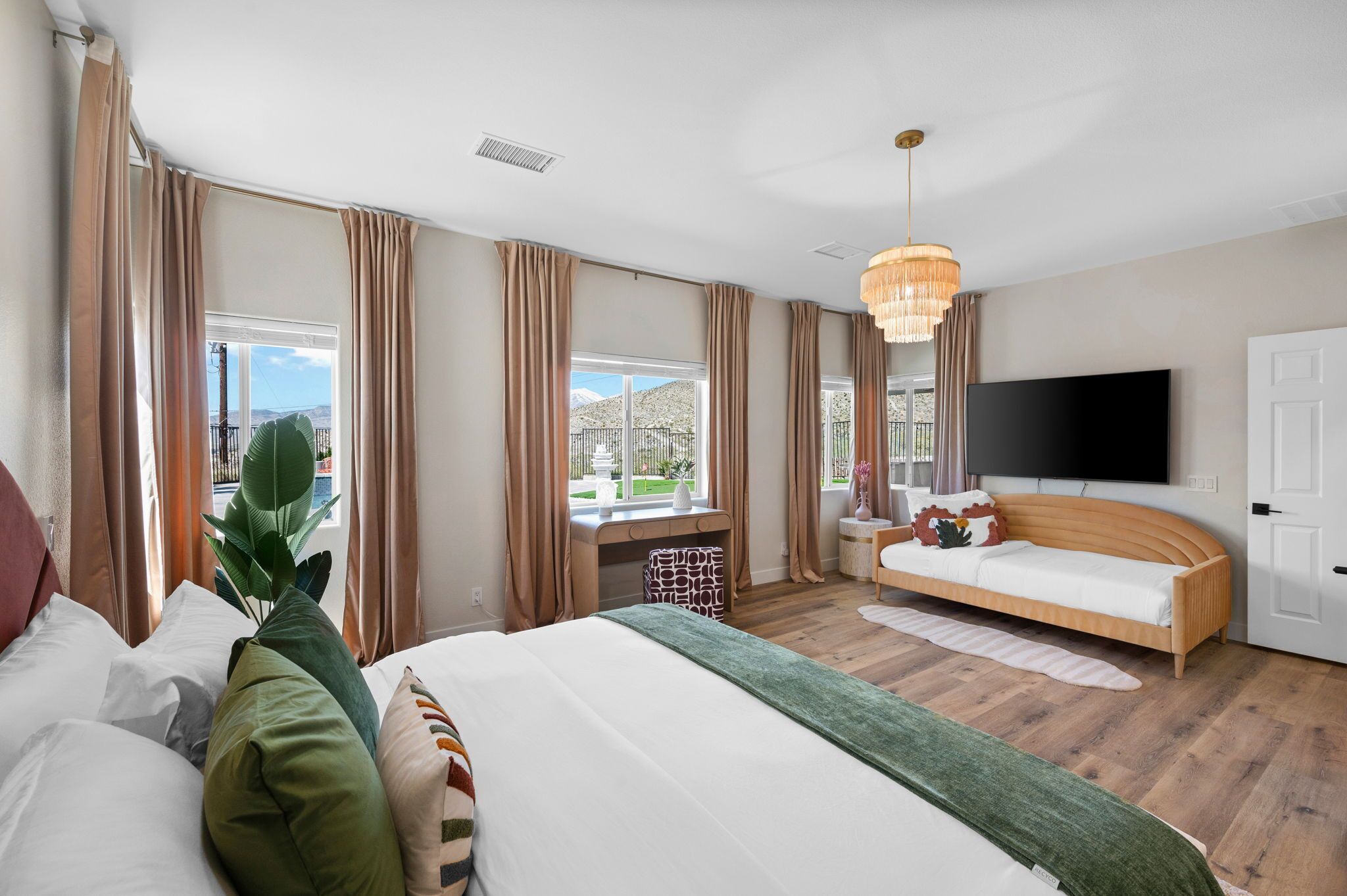 A bedroom with a bed, a sofa, a TV, and large windows with curtains.