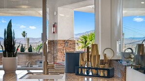 Una cocina con encimeras de granito, un lavamanos y vistas a montañas a través de amplios ventanales.