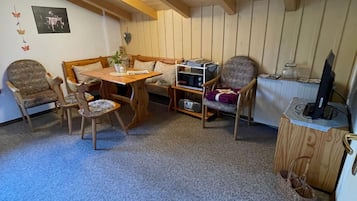 Ein gemütliches Zimmer mit Holzbalkendecke, einem Esstisch mit Stühlen, einer Mikrowelle und einem Fernseher.