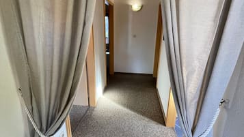 A corridor with a carpeted floor, wooden ceiling beams, and curtains tied at the bottom.