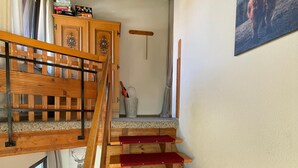 Un escalier en bois, dont les marches sont recouvertes d’une moquette rouge, mène à une mezzanine.
