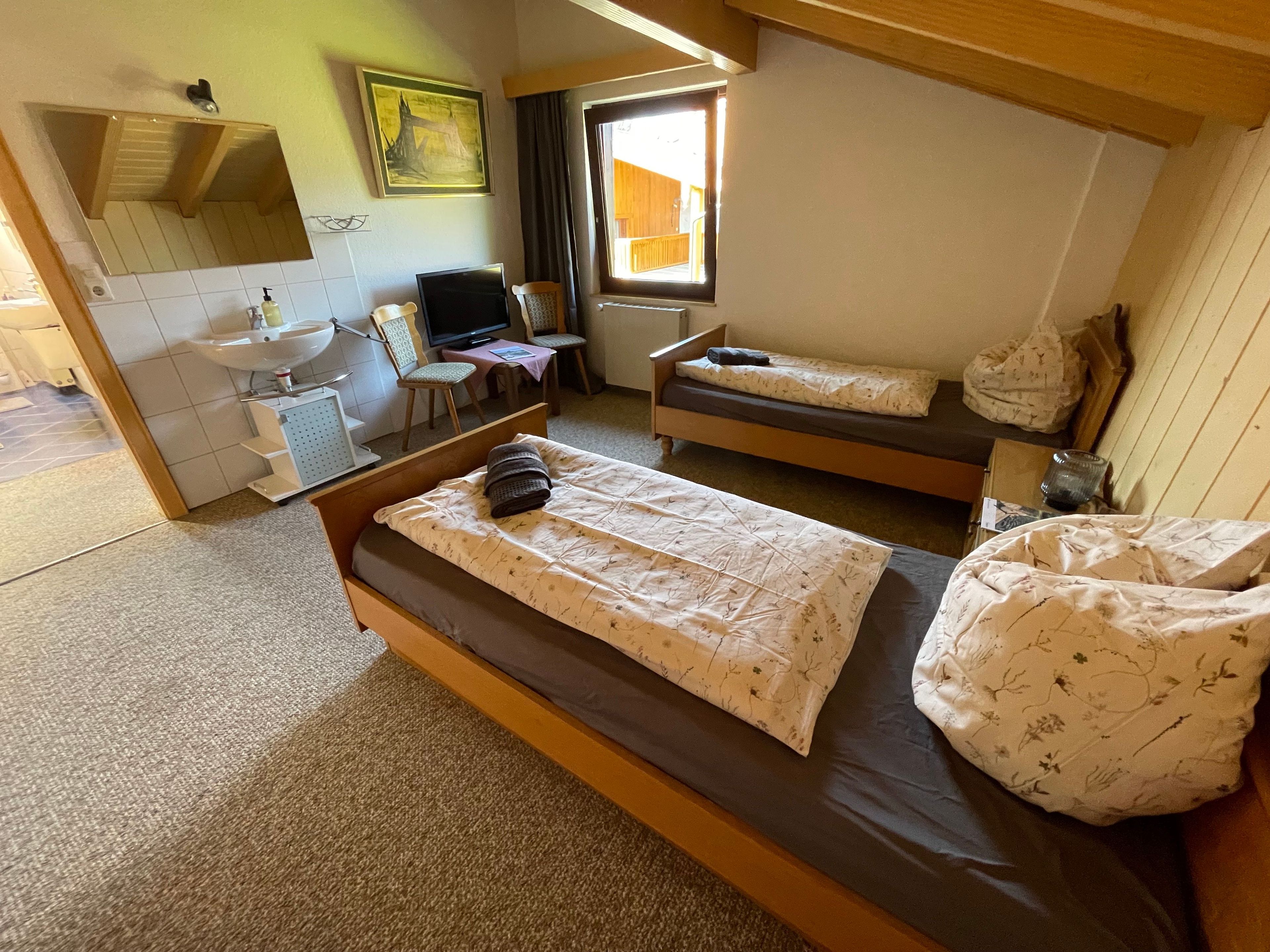 Een kamer met twee bedden, een bureau met een computer, een raam en een badkamer.