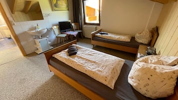 Een kamer met twee bedden, een bureau met een computer, een raam en een badkamer.