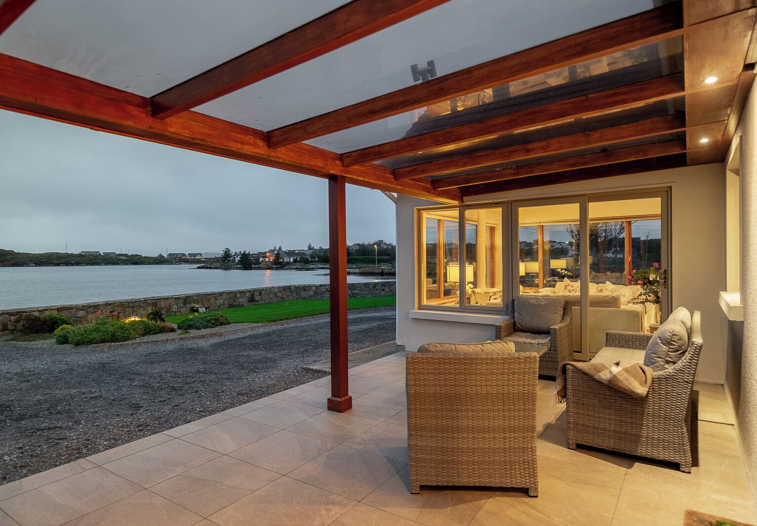 A covered patio with wicker furniture, a stone wall, and a view of the water.