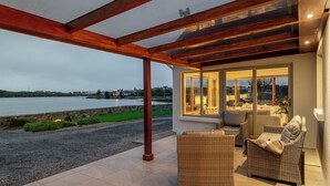 En overdækket terrasse med fletningsmøbler, en stenvæg og udsigt til vandet.