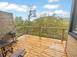 Une terrasse en bois avec une rambarde en métal, un barbecue et une table avec des chaises.