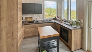 A modern kitchen with wooden cabinetry, a built-in oven, a large window, and a view of the outdoors.
