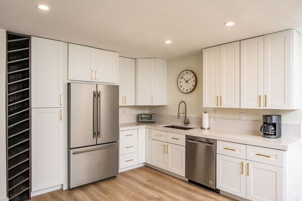 Una cocina moderna con armarios blancos, electrodomésticos de acero inoxidable y un reloj en la pared.