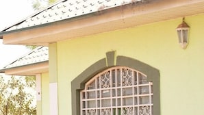 Ein Gebäude mit einem Ziegeldach, einem großen, dekorativen Fenster mit Gittermuster und einer kleinen Veranda mit Stufen.