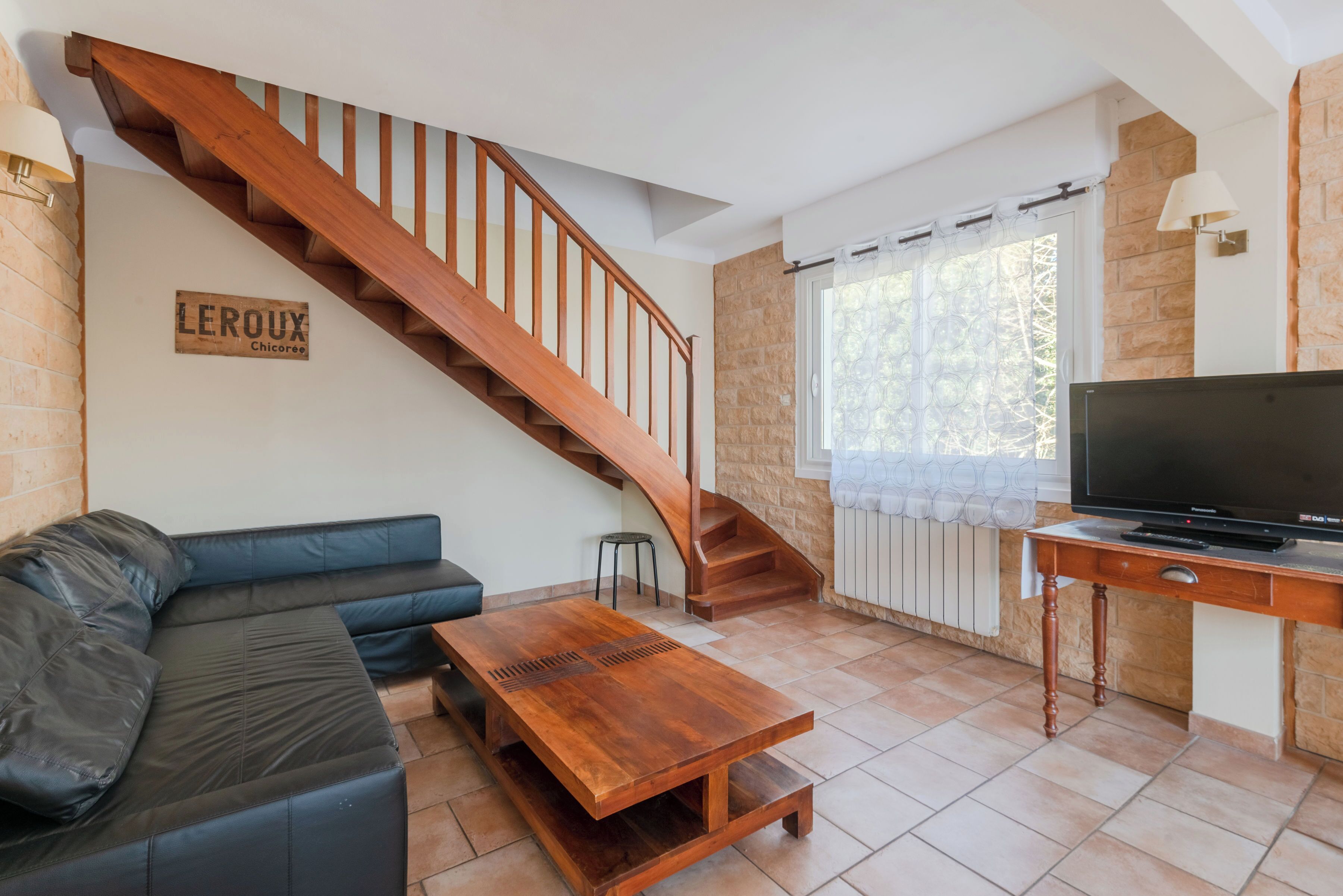 Ein Wohnzimmer mit einer Holztreppe, einem schwarzen Ledersofa, einem Couchtisch aus Holz und einem Fernseher auf einem Holzschrank.