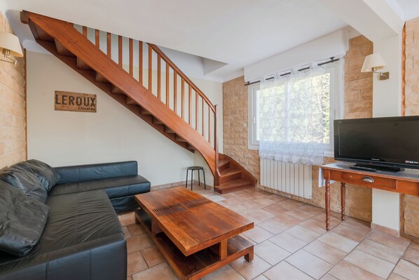 A living room with a wooden staircase, a black leather sofa, a wooden coffee table, and a television on a wooden stand.