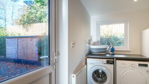 Une buanderie équipée d’un lave-linge et d’un sèche-linge, une fenêtre donnant sur une clôture en bois et un radiateur.