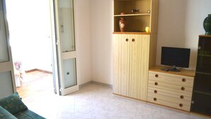 Ein Zimmer mit einer Couch, einem Fernseher auf einer Holzeinrichtung und einer Schiebetür zu einem weiteren Raum.