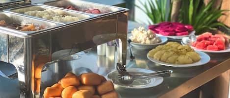 A buffet with various food items including rice, meat, potato salad, and watermelon slices.
