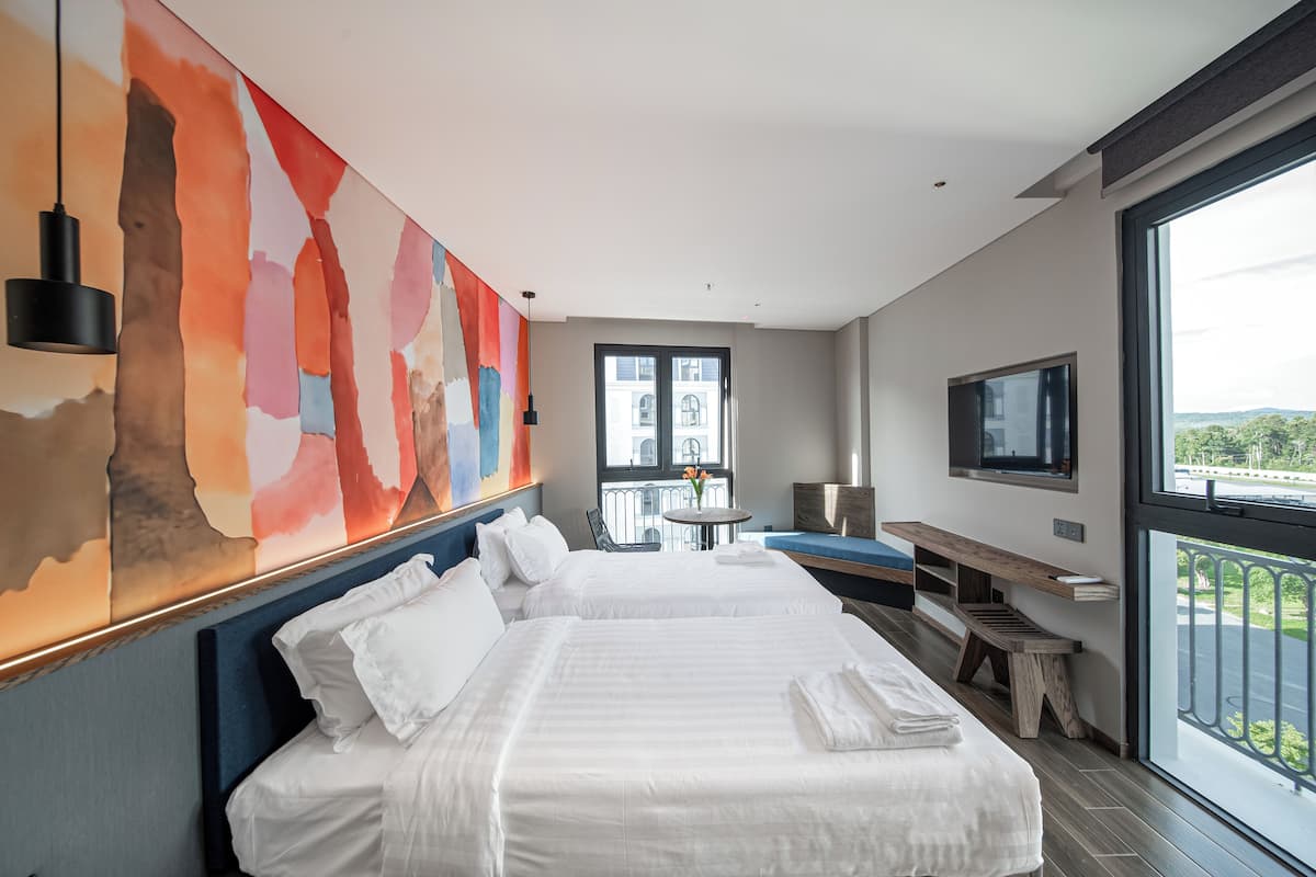 Una habitación de hotel moderna con dos camas, un ventanal grande, un televisor y un cuadro abstracto de colores en la pared.