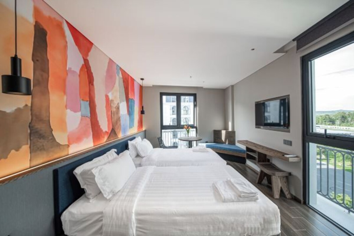 Habitación de hotel moderna con una cama grande, un escritorio, un televisor y un balcón con vistas.