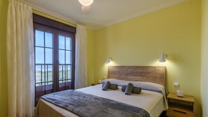 Un dormitorio con una cama grande, dos mesitas de noche, un cabecero de madera y vistas a través de una ventana con cortinas.