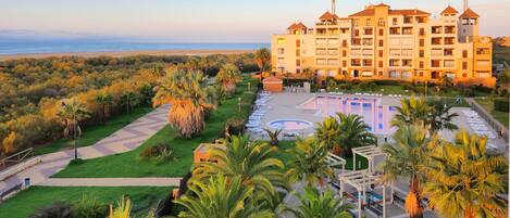 A hotel with a pool, palm trees, and a view of the beach.