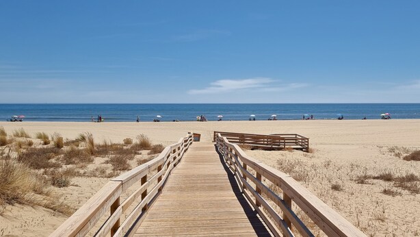 Una pasarela de madera que lleva a una playa con cielos despejados.