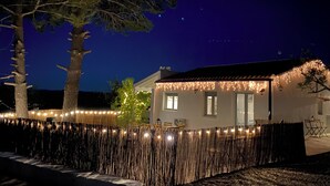 A house with a white exterior, a red roof, and a wooden fence. There are string lights along the fence and a tree in the foreground. - Casa the Dutchman,  totally off-grid,on a private plot of 10.000m2 (Navarres)