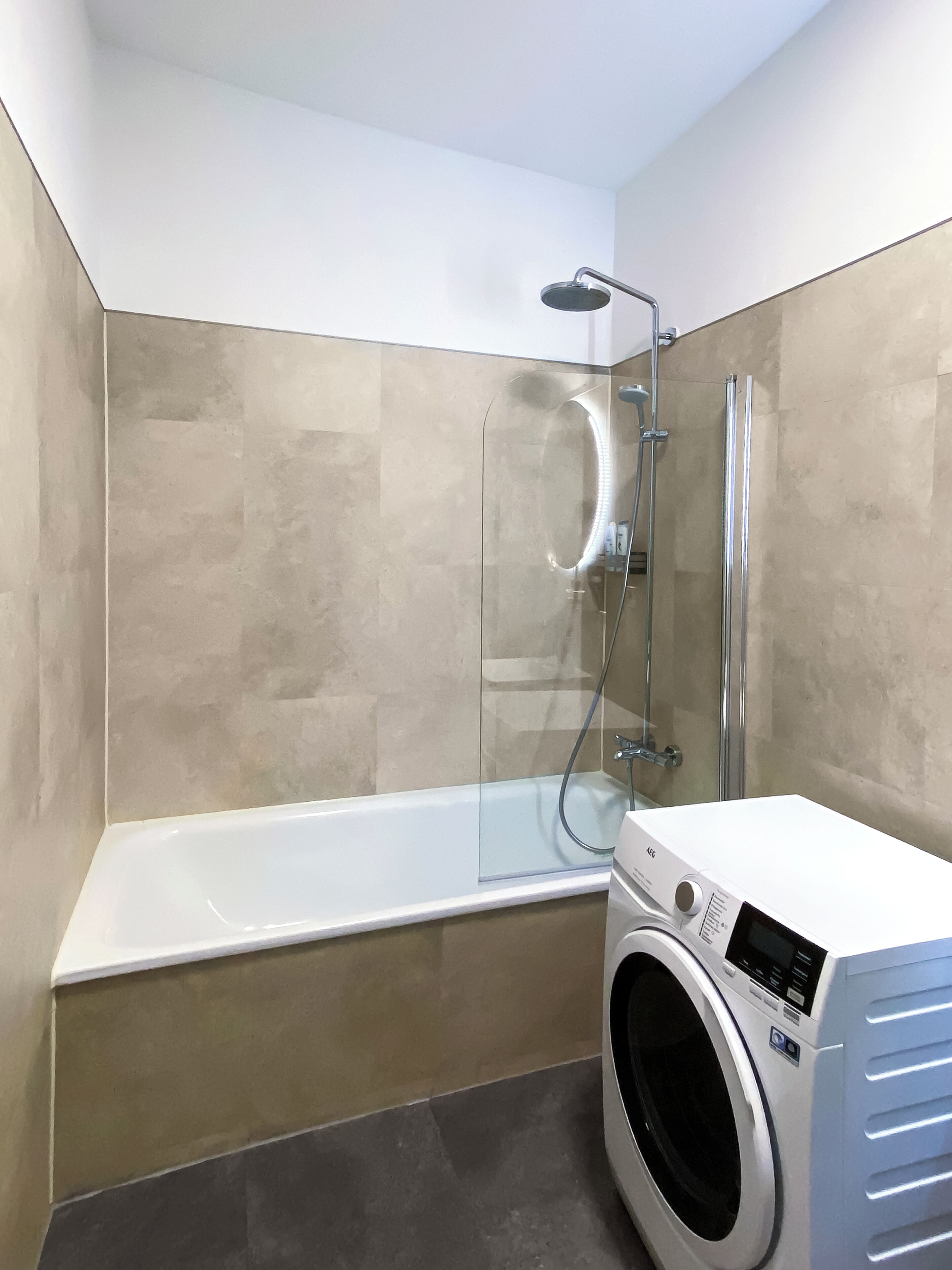 A modern bathroom with a glass-enclosed shower, a white bathtub, and a front-loading washing machine.