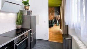 A modern kitchen with a built-in oven, microwave, and refrigerator. There is a potted plant on the counter and a trash can near the window. - Exklusives City Apartment Nature (Leipzig)