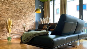 A modern living room with a black leather sofa, a green ceiling, and a brick wall. - Exklusives City Apartment Nature (Leipzig)