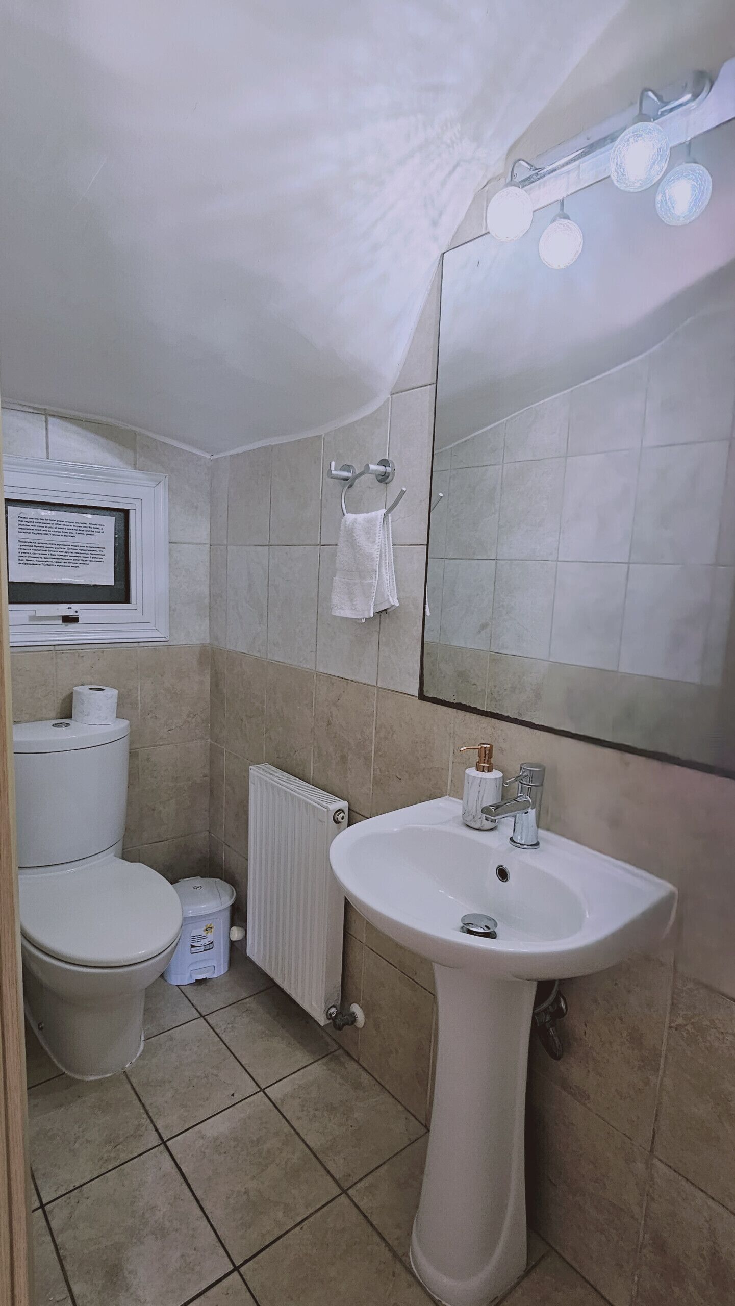Een badkamer met een witte wastafel, toilet en spiegel. Er hangt een handdoek aan de muur en eronder staat een radiator.