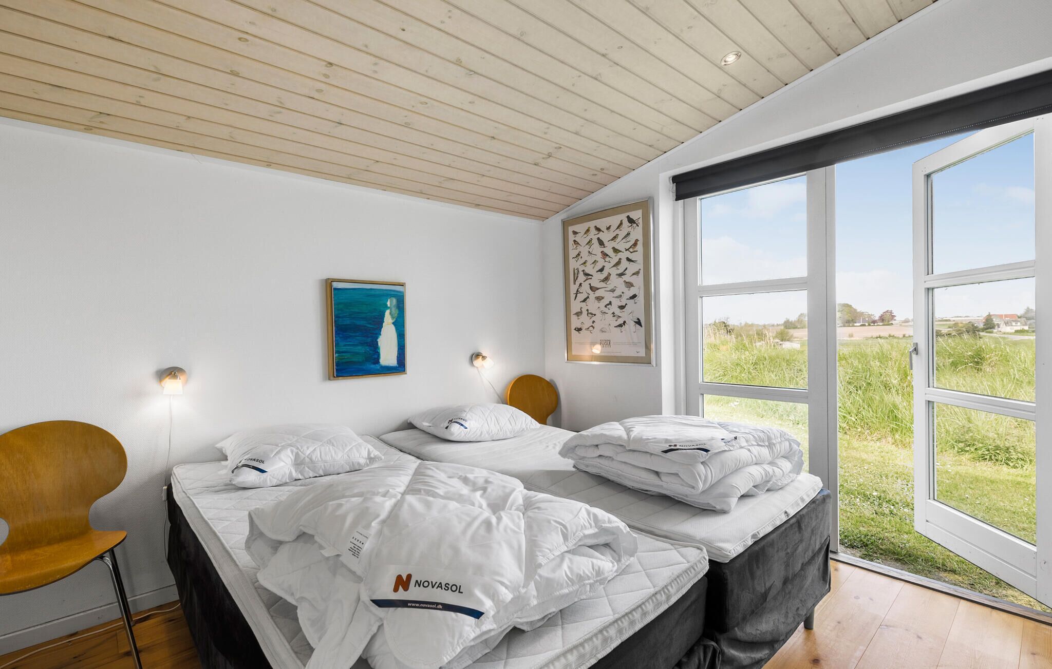 Une chambre à coucher avec un lit, un plafond en bois, une grande fenêtre et un mur orné d’une illustration d’oiseau.