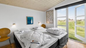 Une chambre à coucher avec un lit, un plafond en bois, une grande fenêtre et un mur orné d’une illustration d’oiseau.