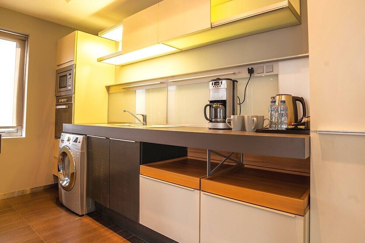 A compact kitchen with a washing machine, a coffee maker, and a kettle on the counter.