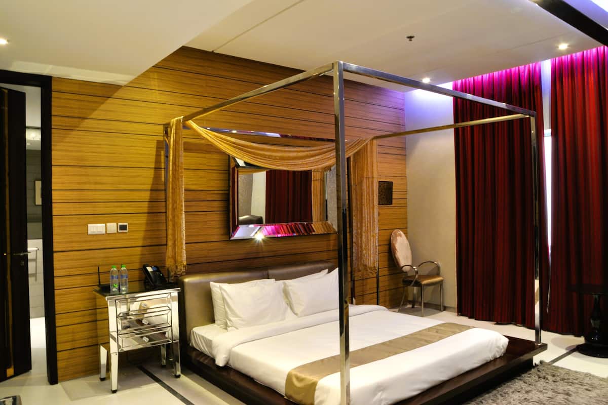 A modern hotel room with a four-poster bed, wooden paneling, a vanity with a mirror, and a red curtain.