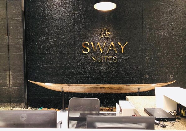 A reception desk area with a black textured wall, a wooden boat decoration, and a Dell computer. - Sway Suites (Manama)
