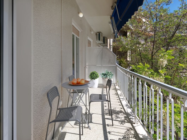 A balcony with a table, chairs, and a potted plant.